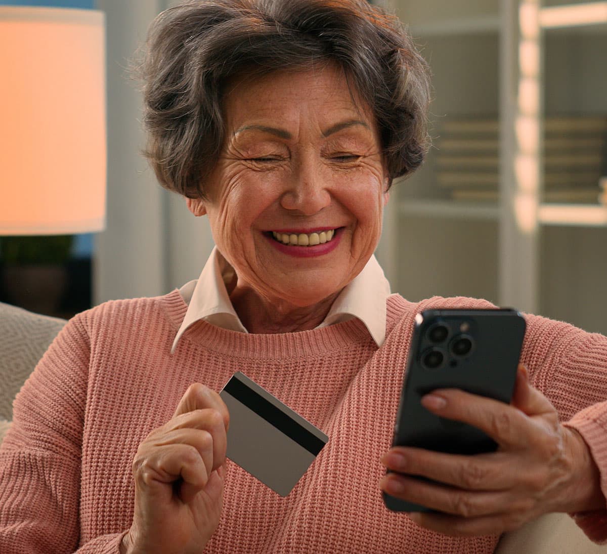 Happy senior woman sitting on a sofa with credit card looking at her phone